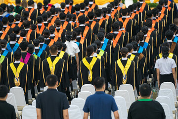 Fototapeta premium Rear view of university graduates wearing graduation gowns and caps in the commencement day in the hall.