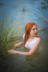 Redhead girl walking on the river shore and posing in the water.