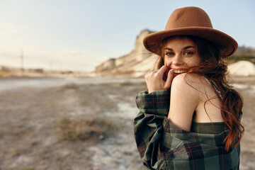 Woman in stylish hat and plaid shirt striking a pose in the arid desert landscape