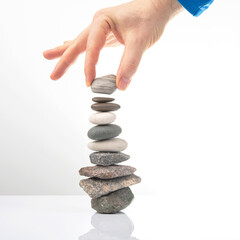 hand builds a pyramid from stacked stones on a white background. stabilization and balance in life