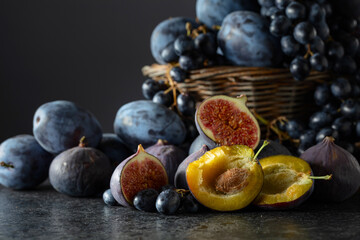 Blue grapes, blue plums, and figs on a black stone table.