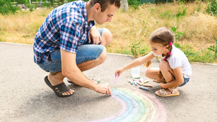 Father and his little daughter drawing together with chalks on street in summer