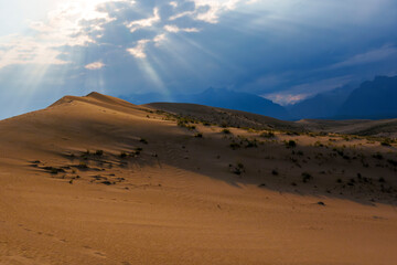 Dramatic desert dunes under sunbeams and cloudy sky