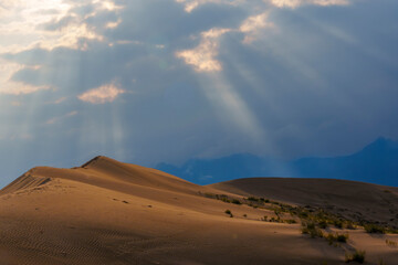 Dramatic desert dunes under sunbeams and cloudy sky