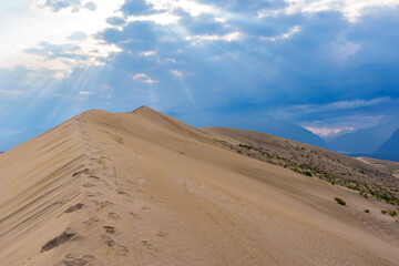 Dramatic desert dunes under sunbeams and cloudy sky
