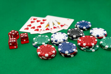 Multicolored Poker chips and dice with royal flush in hearts on green table