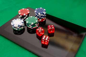 Stacks of Poker Chips and Red Dice on a Digital Tablet on green felt background