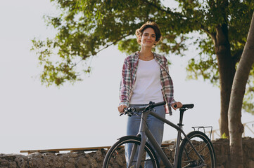 Young happy smiling woman she wearing shirt casual clothes walking strolling with bicycle in green...