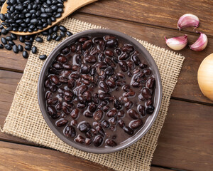 Cooked black beans in a bowl over wooden table with onion and garlic