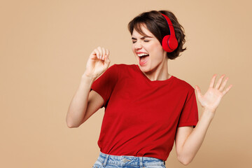 Young smiling happy woman she wear red t-shirt casual clothes listen to music in headphones sing...