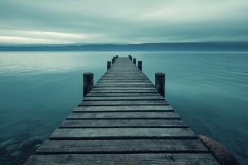 Fototapeta premium A long wooden pier stretching out into calm and serene blue waters under a soft cloudy sky, evoking tranquility.