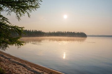 Sunrise over a misty forest lake with sandy shoreline