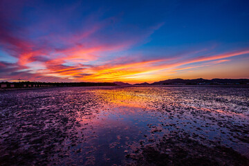 Sunset view of mud flat at low tide at Jomnaru Beach against red glow in the sky at Songhyeon-ri near Muan-gun, South Korea 