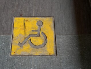 Yellow wheel chair icon isolated on horizontal outdoor gray stone ramp flooring texture background.