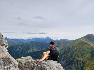 Hiker is resting on a rock on top of a mountain enjoying the view of a valley,  view from Giewont, Tatra national park, Poland