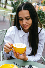 Beautiful brunette holds  yellow coffee mug with milk foam.