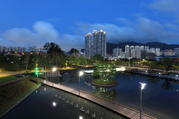 Busanjin-gu, Busan, South Korea - August 20, 2021: Night and aerial view of trail and pond against high-rise apartments at Busan Citizens Park