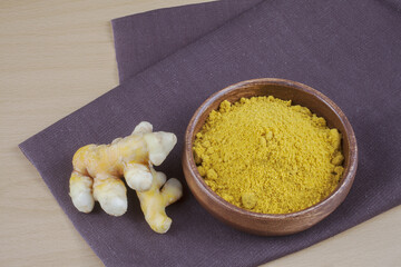 Close-up of trimmed roots of turmeric and curcuma with yellow curry powder in wooden bowl on cloth, South Korea