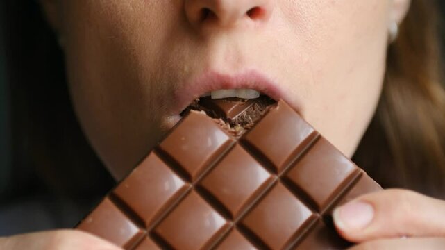 Woman holds chocolate bar bitting small piece of sweet snack. Female enjoys delicious taste of dessert experiencing satisfaction after strict diet