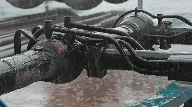 Heavy industrial equipment on a pipeline with visible connections and joints, highlighted under rainy weather, illustrating the complexity and robustness of infrastructural components.