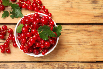Fresh red currants and green leaves on wooden table, top view. Space for text