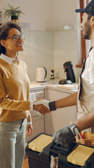 Professional repairman in uniform shaking hands with woman while standing at home kitchen