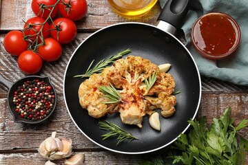 Tasty cauliflower steak in frying pan and other products on wooden table, top view