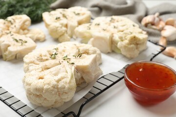 Uncooked cauliflower steaks and sauce on white table, closeup