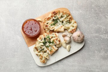Delicious grilled cauliflower steaks with sauce and garlic on grey table, top view