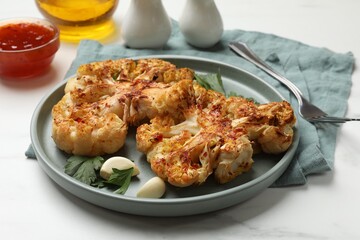 Delicious baked cauliflower steaks with garlic and parsley on white table, closeup