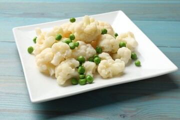 Tasty cooked cauliflower with green peas on light blue wooden table, closeup