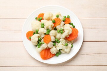Tasty cooked cauliflower with green peas and carrot slices on white wooden table, top view
