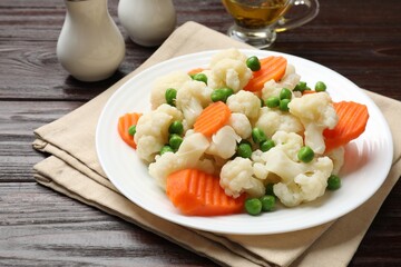 Tasty cooked cauliflower with green peas and carrot slices on white wooden table, closeup