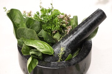 Different aromatic herbs in mortar on white table, closeup