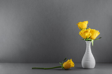 Bouquet of yellow roses in a small ceramic vase on a gray background. Congratulatory background with copy space. © Natalia