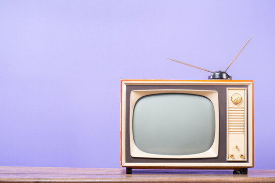 TV with retro old antenna on table front purple background. Vintage style filtered photo
