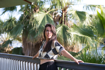 young and beautiful Latin woman on holiday is resting leaning on the iron railing, in the...