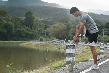 A young man pauses by a lakeside, securing his shoelace on a pole, surrounded by lush greenery and...