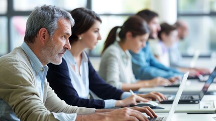 Adults in a computer lab, each working on a laptop and following the instructorâ€™s demonstration