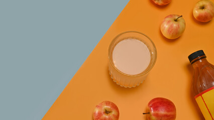 A glass of apple cider vinegar, fresh apples, and a bottle of vinegar arranged against a backdrop of blue and orange, blending nature with simplicity in a modern aesthetic, Top view