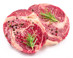 Raw beef steaks with herbs and spices ready for cooking on white background.