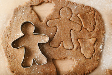 Cooking ginger cookies, Christmas and New Year traditional cookies in shape of gingerbread man, raw rolled out dough with cut out dough figures, closeup texture, top view, metal pastry cutter on dough
