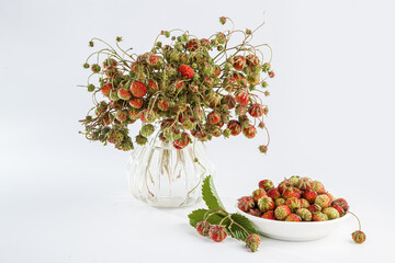 A bouquet of wild strawberries in a transparent vase on a white background