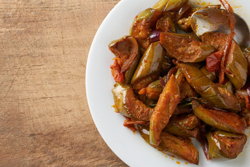 close-up of eggplant dish on wooden surface, golden and crispy fried brinjal mixed with tempered spices with flavors of sweet, sour and spicy taste, taken from above with copy space