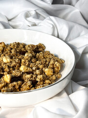 Granola with nuts and raisins in a white plate close-up on a white textile background. Top view. Healthy proper breakfast.