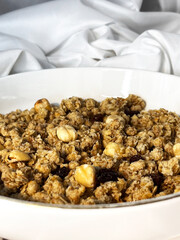Granola with nuts and raisins in a white plate close-up on a white textile background. Top view. Healthy proper breakfast.