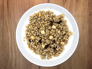 Granola with nuts and raisins in a white plate close-up on a wooden background. Top view. Healthy proper breakfast.