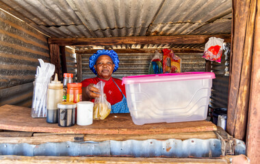 tuck shop , african woman in a shack selling chips, French fries , street vendor with small business in a village spaza , fast food