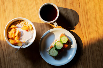 Healthy breakfast: oatmeal with yogurt and peach, salmon crackers, cream cheese, cucumber, and black coffee.