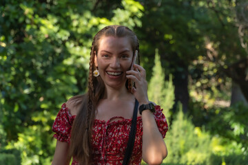 Sunlit Serenity: Redhead Enjoys a Carefree Walk While Chatting on Her Phone in a Lush Garden